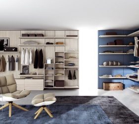 cabina armadio di lusso in legno con scaffali a vista che occupa tutte le pareti e al cui centro si trova una poltrona con pouf