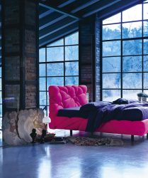 camera da letto in un ambiente in stile industriale con ampia vetrata che illumina un letto rosso di design con imbottitura