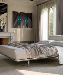 camera da letto elegante bianca illuminata da ampie finestre con camino e poltrona