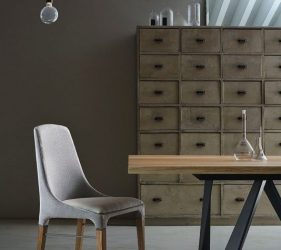 dettaglio di una sedia di design in legno e pelle con tavolo in legno e ferro, sullo sfondo un grande armadio a cassetti